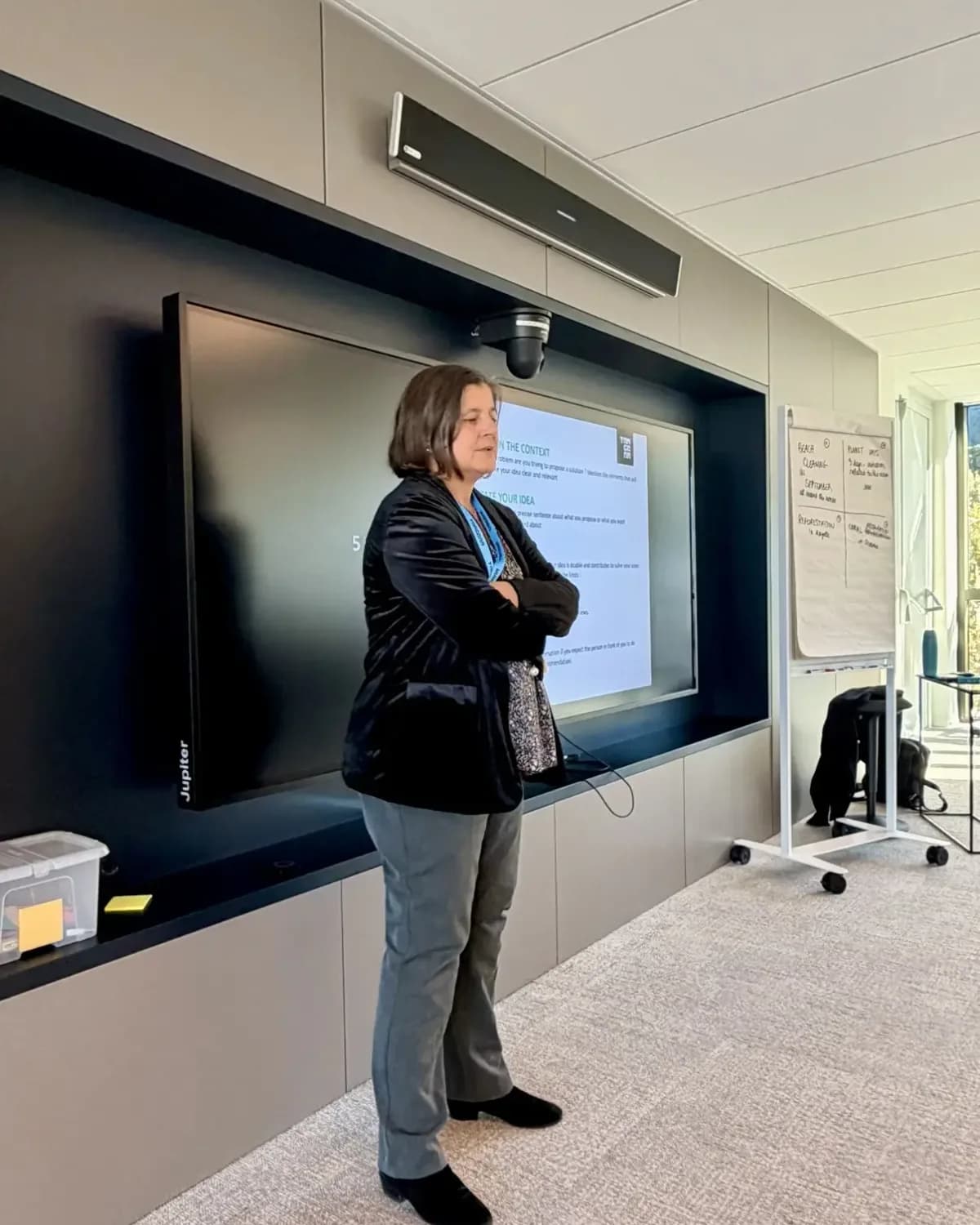 Vera Ingallati facilitating a working session beside a presentation screen, flip charts of the group's ideas standing to one side.